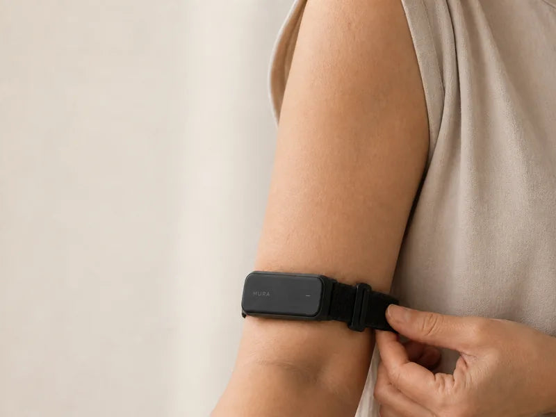 Illustrative close-up of a Carbon Mura Band on an upper arm, with a hand adjusting the woven strap