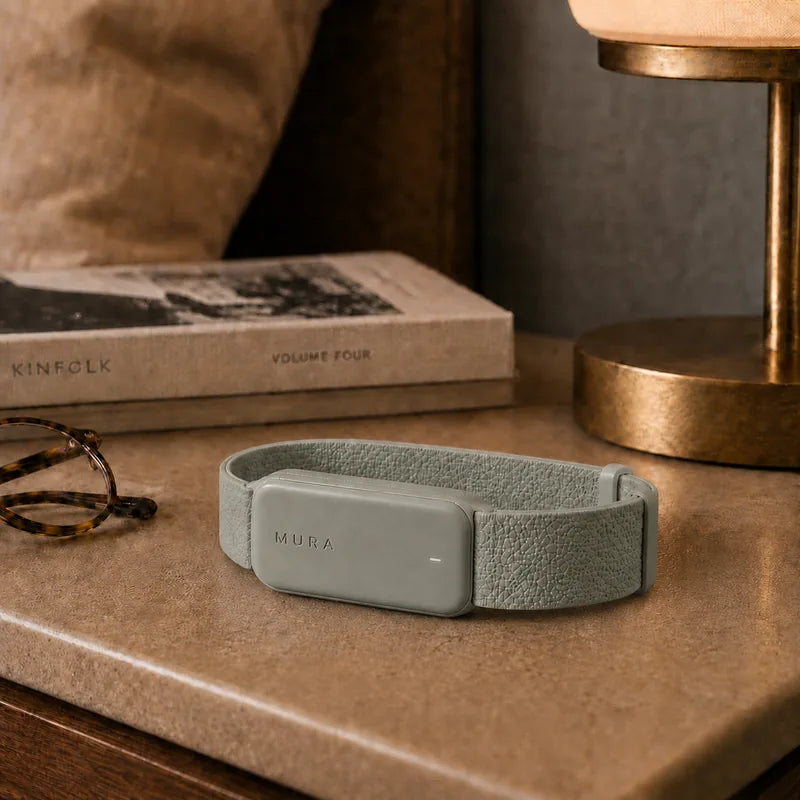 Mura wearable resting on a bedside table beside books and a lamp